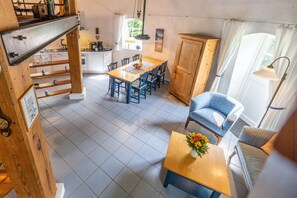 A dining area with a wooden table, blue chairs, a cabinet, and a sofa. - Holiday Home 'Windmill Betty by the North Sea' with Private Terrace, Private Garden and Wi-Fi (Cuxhaven)