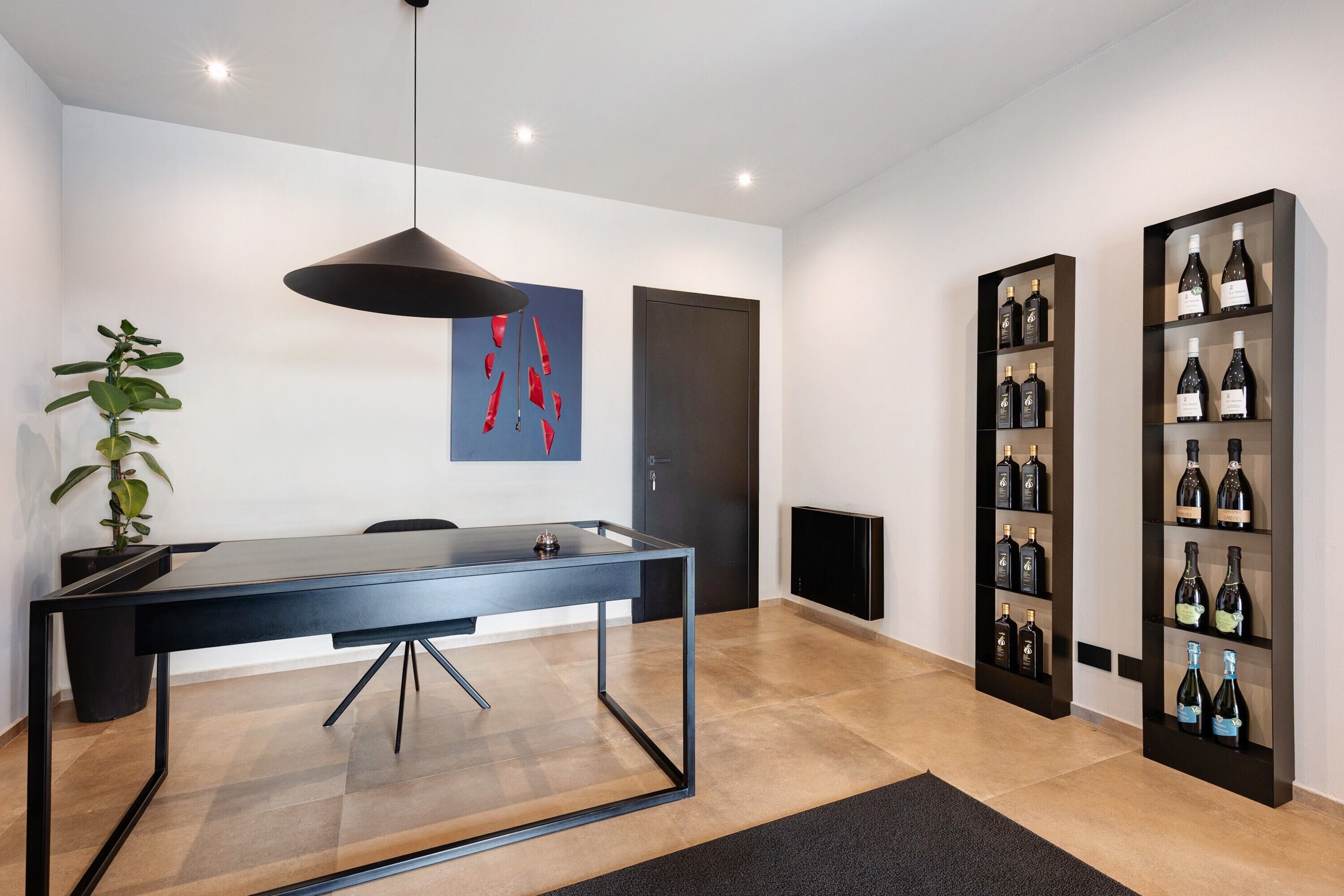 A modern dining area with a black table, chairs, a pendant light, a potted plant, and wine shelves.