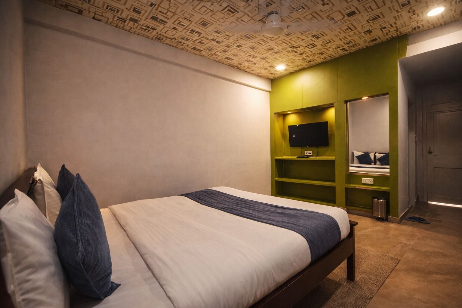 A bedroom with a bed, pillows, a TV on a shelf, and a mirror.