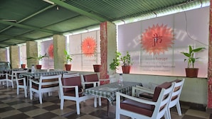 Un restaurante con piso a cuadros, sillas blancas y mesas con manteles escoceses. Hay plantas en macetas sobre las mesas y un letrero grande con texto y un diseño floral.
