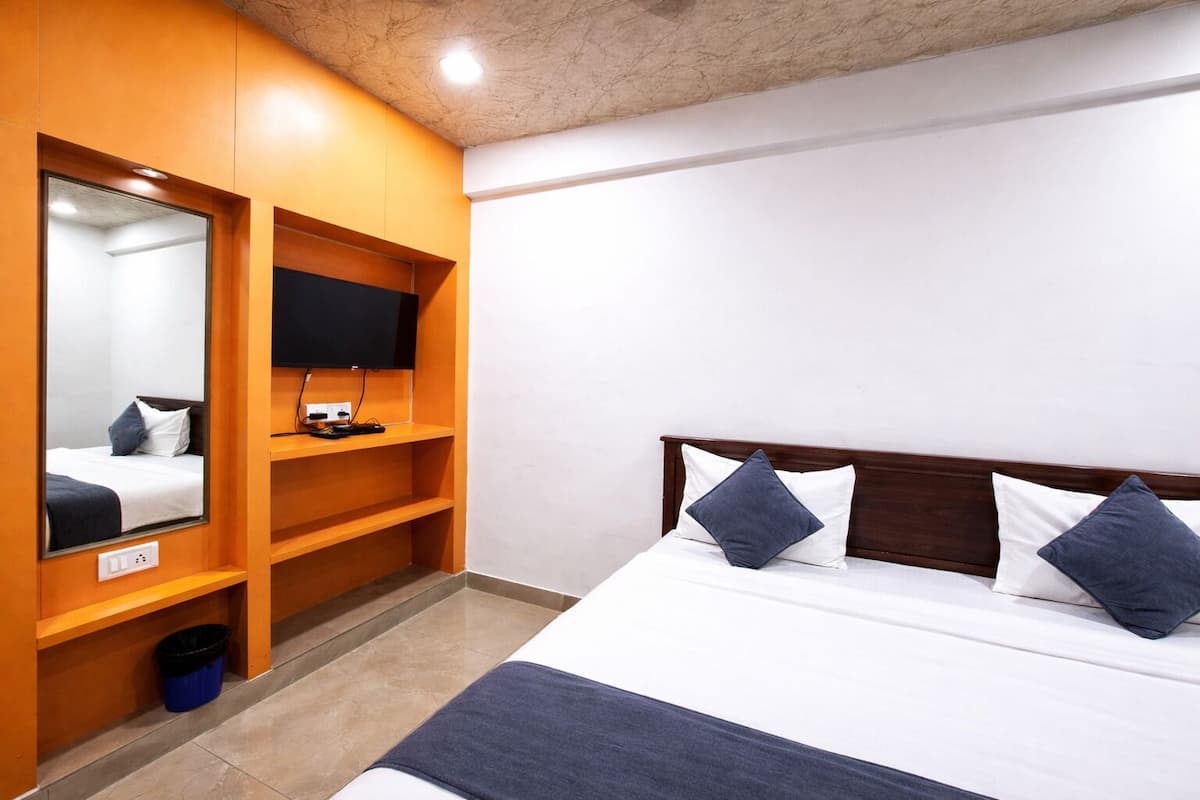 A hotel room with a bed, a TV mounted on a wooden shelf, and a mirror.