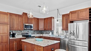 Eine moderne Küche mit Holzschränken, Edelstahlgeräten, einer Granitabdeckung und Pendelleuchten.