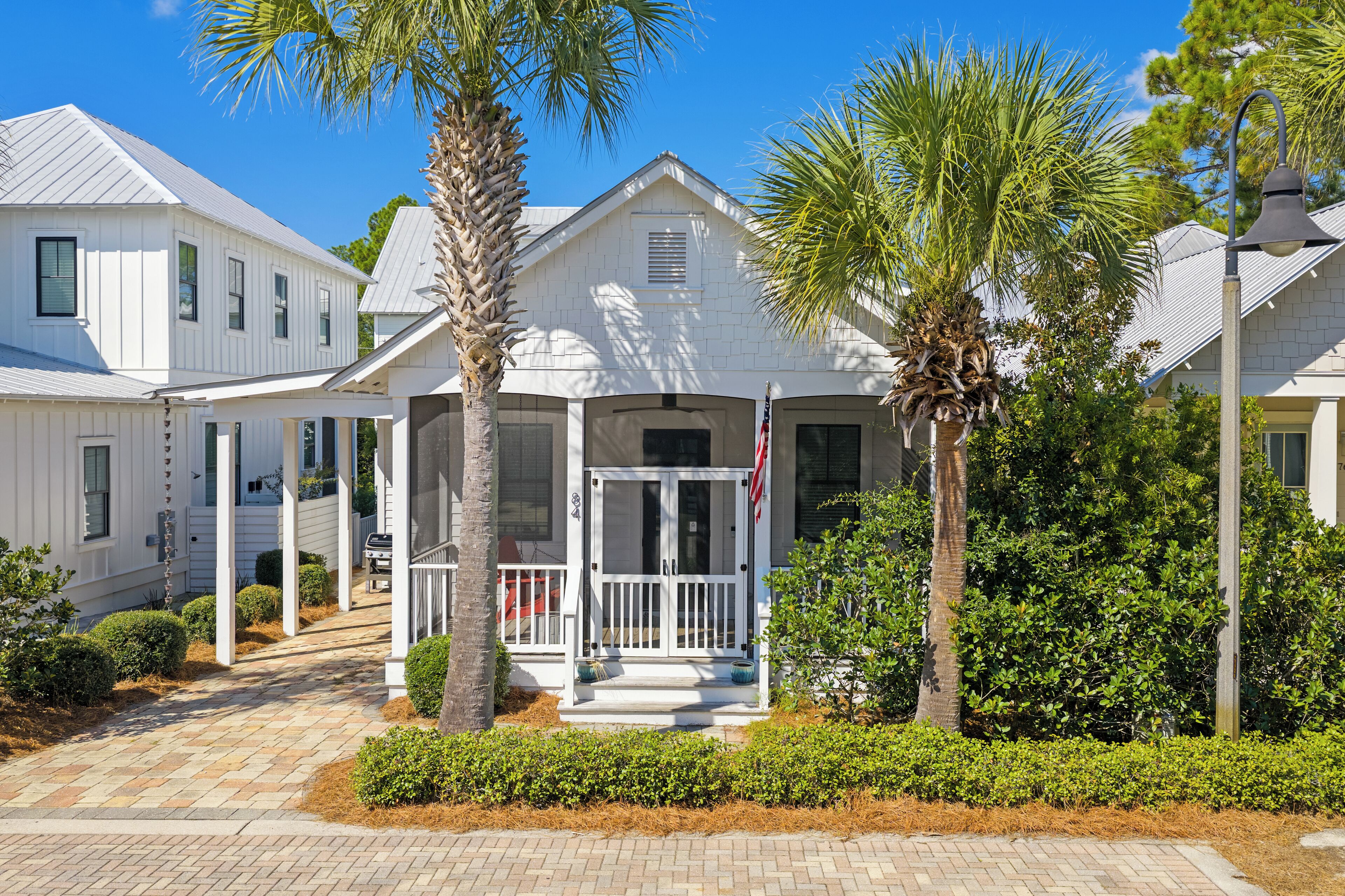 A white two-story house with a covered porch, palm trees, and a well-maintained garden.