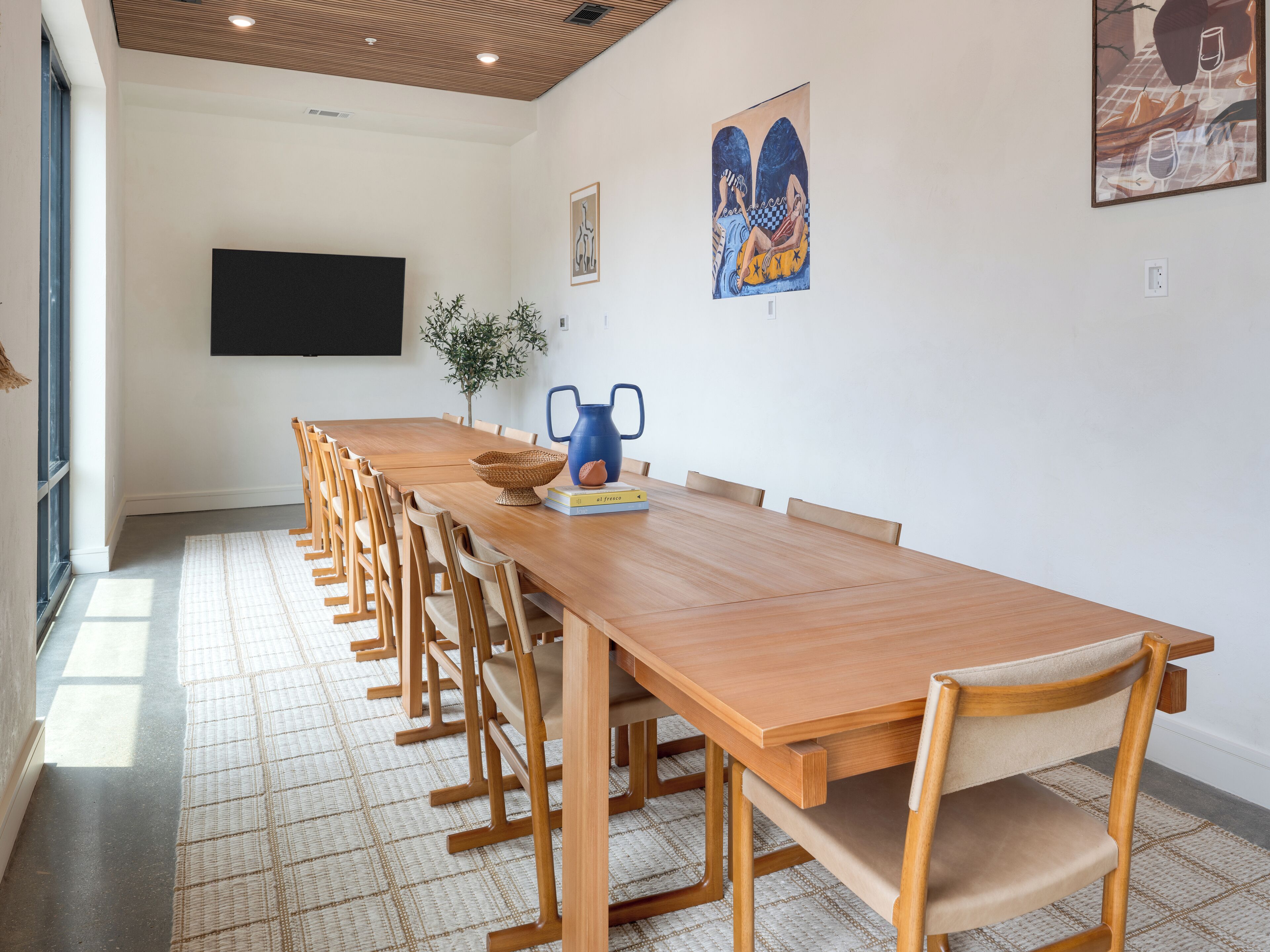 Een lange houten tafel met stoelen, een plant en kunstwerken aan de muur.