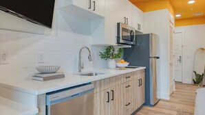 A modern kitchen with white cabinetry, a stainless steel dishwasher, a microwave, and a refrigerator. - Brand New Modern Stay In 12 South | The Gilmore (Nashville)