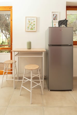 Una cucina con un frigorifero in acciaio inox, un tavolo di legno, due sgabelli in vimini e un quadro appeso al muro.