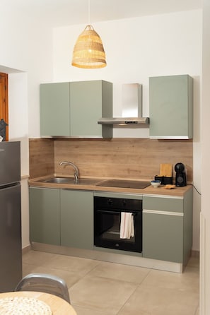 Una cucina compatta con un piano di lavoro in legno, forno integrato e lampada a sospensione.