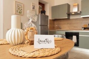 Une cuisine avec un set de table en fibres tressées, un sachet de biscuits Quaresimali, un vase et une carte de remerciement.