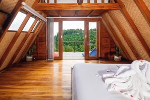 Un dormitorio en el ático con techo de madera, una cama, un balcón y plantas en macetas.