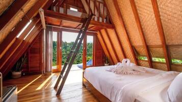 Una habitación con techos altos, una escalera de madera, una cama con sábanas blancas y vistas al exterior con vegetación.