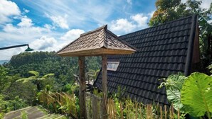 Uma estrutura de madeira tradicional com telhado de telhas, cercada por vegetação exuberante e céu claro.