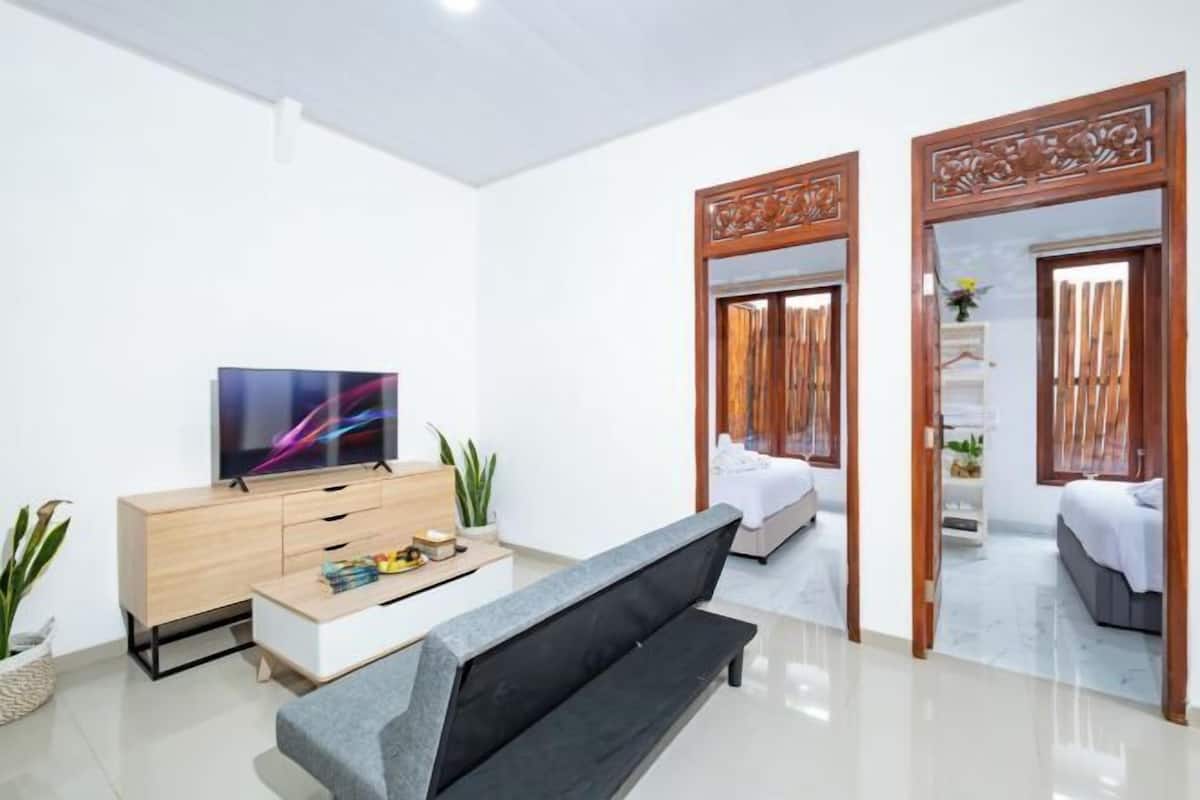A modern living room with a flat-screen TV, a sofa, a wooden cabinet, and a dining table.