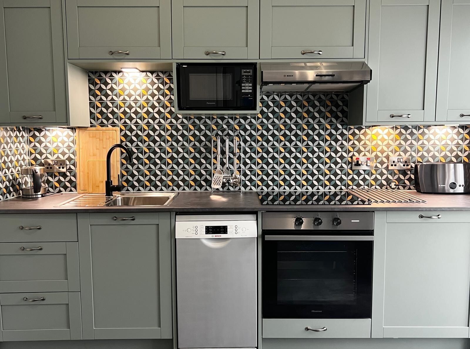 A kitchen with grey cabinets, a Bosch dishwasher, a microwave, a stove, and a toaster.