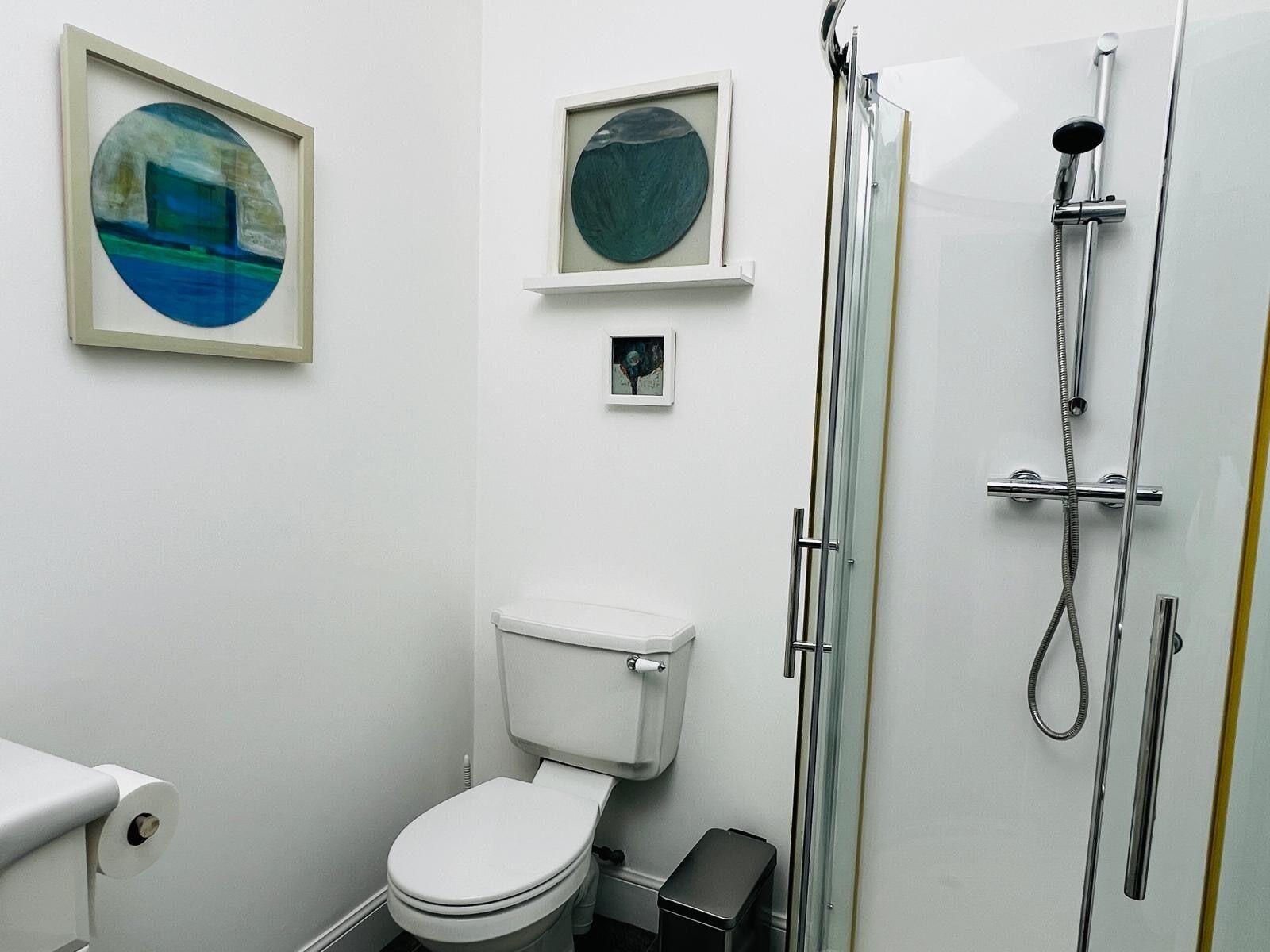 A bathroom with a toilet, a shower, and framed artwork on the wall.