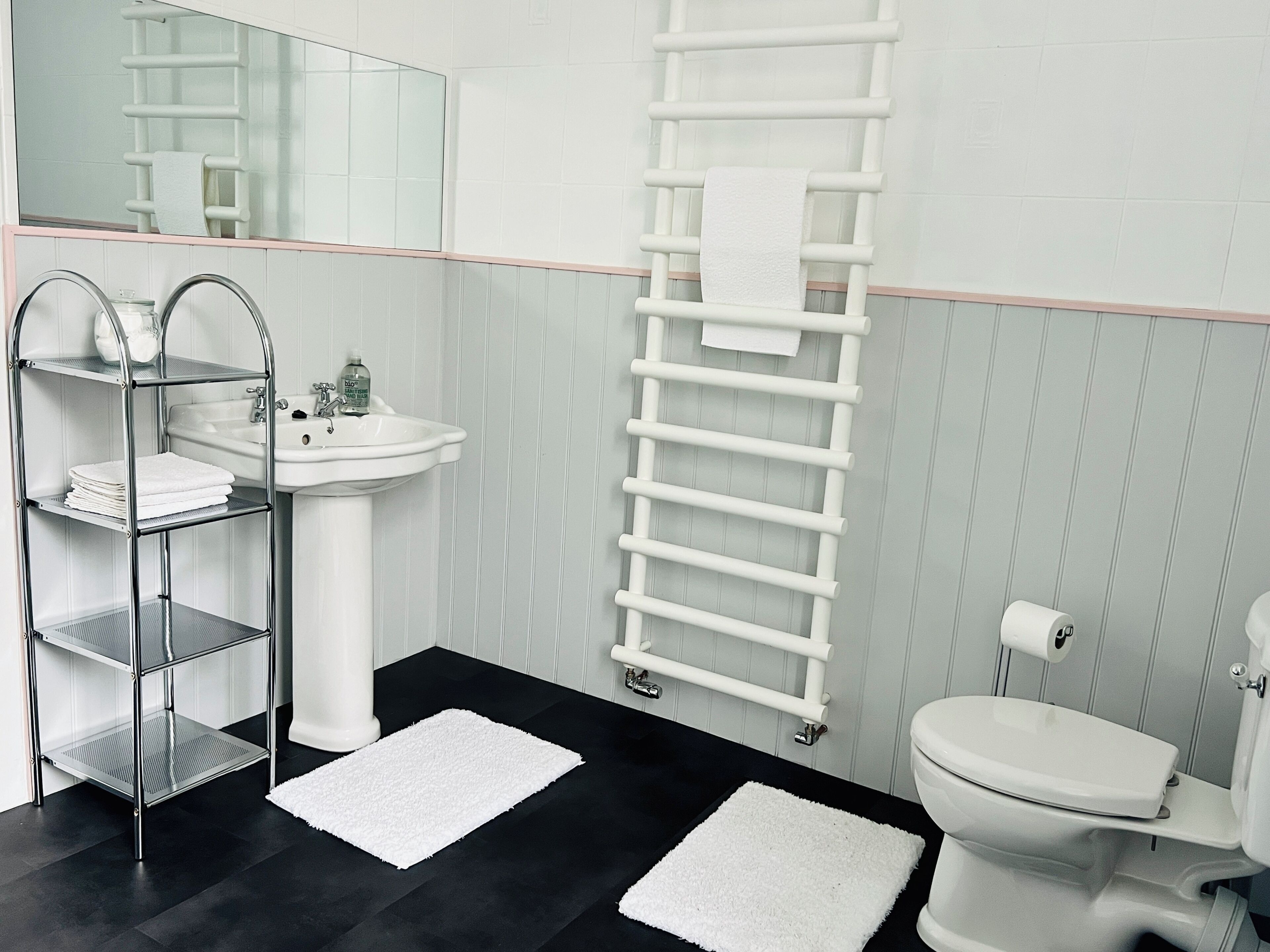 Ein Badezimmer mit Waschbecken, Toilette, Handtuchhalter und einem Metallregal.