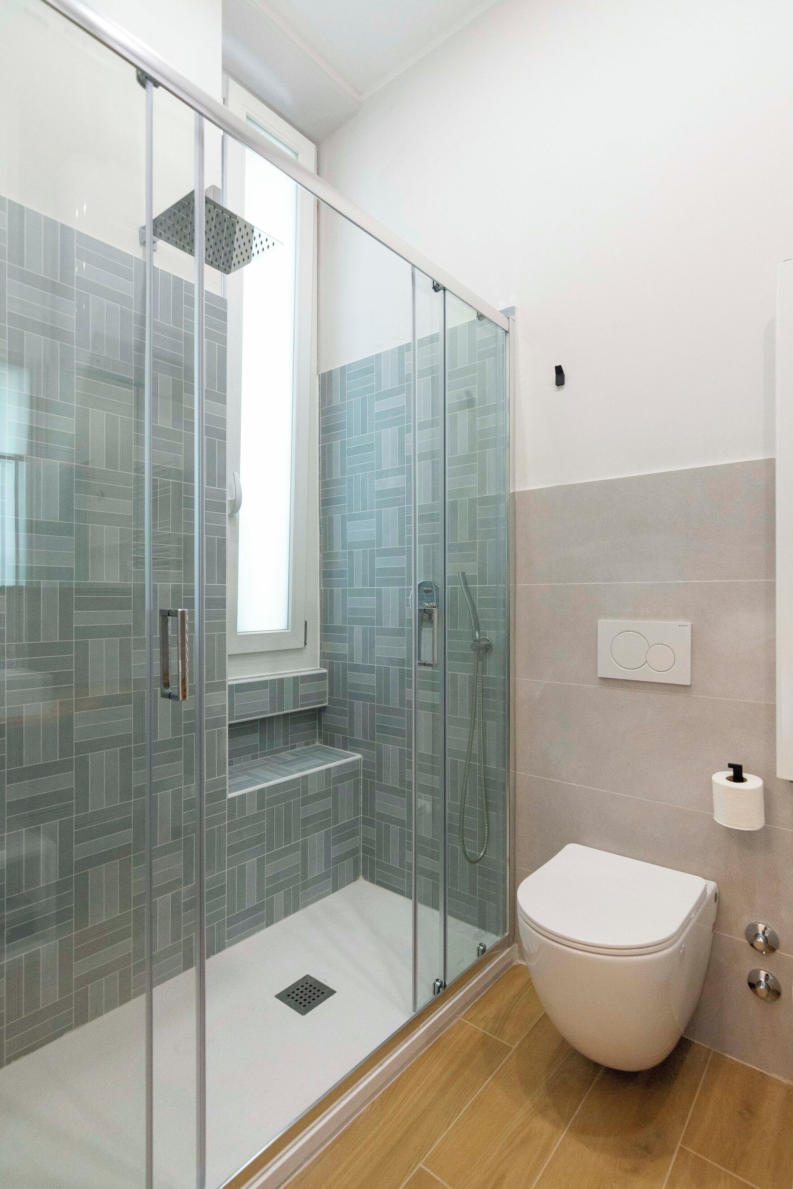 A modern bathroom with a glass-enclosed shower, a white toilet, and a tiled backsplash.