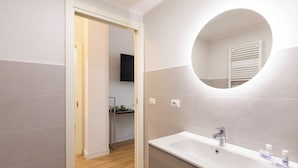 Ein modernes Badezimmer mit einem weißen Waschbecken, einem runden Spiegel und einer Holzkommode.