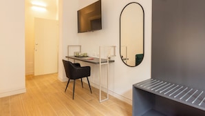 Ein modernes Zimmer mit Schreibtisch, Stuhl, Fernseher und einem großen Spiegel.