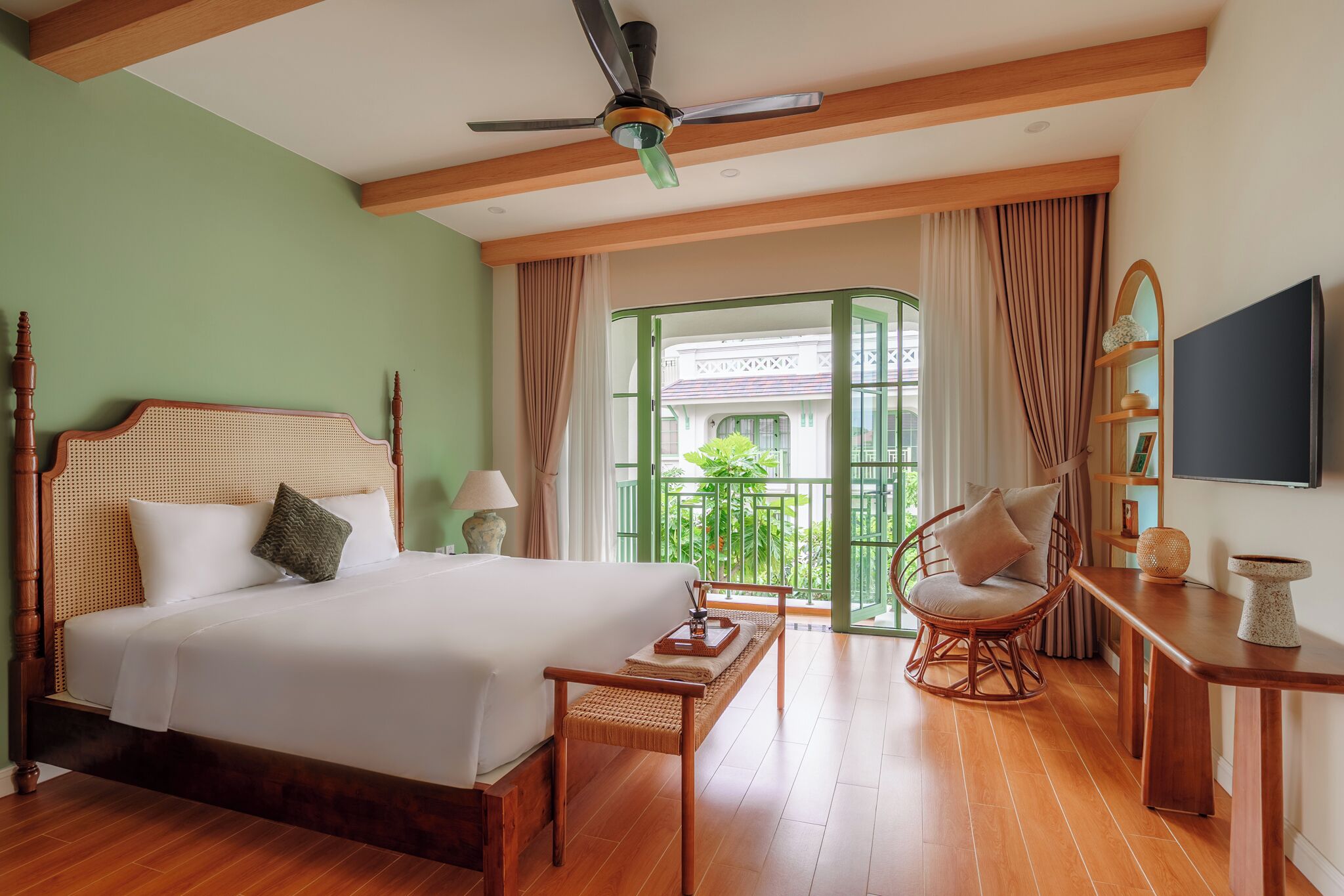 A hotel room with a bed, a chair, a table, a ceiling fan, and a balcony with a view.