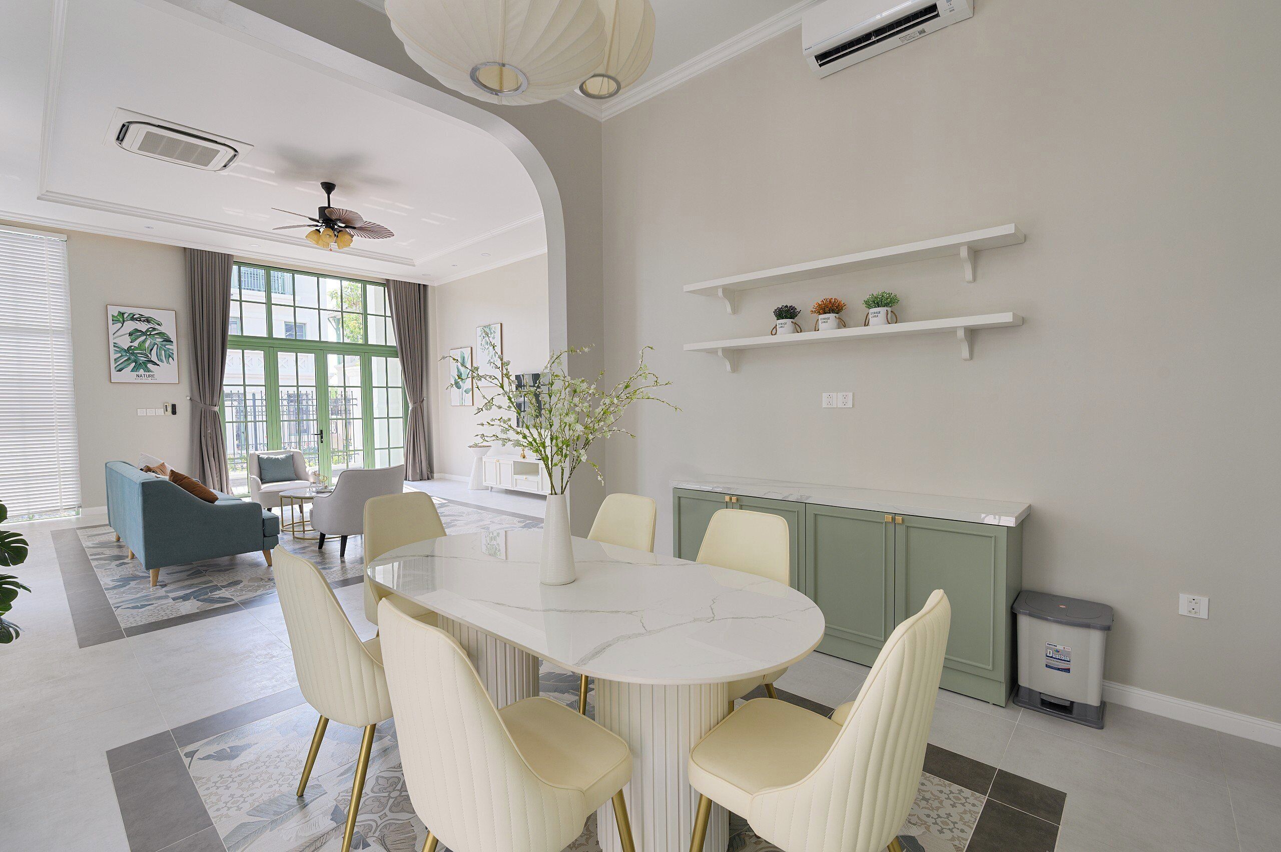 A modern dining area with a white marble table, cream chairs, and a vase with flowers.