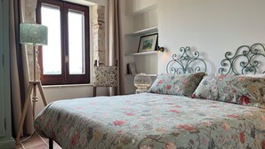 Un dormitorio con colcha estampada, una lámpara de pie, una silla y estructura de cama de metal.