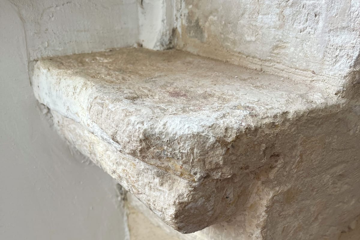 A corner of a room with a textured stone column and a white wall.