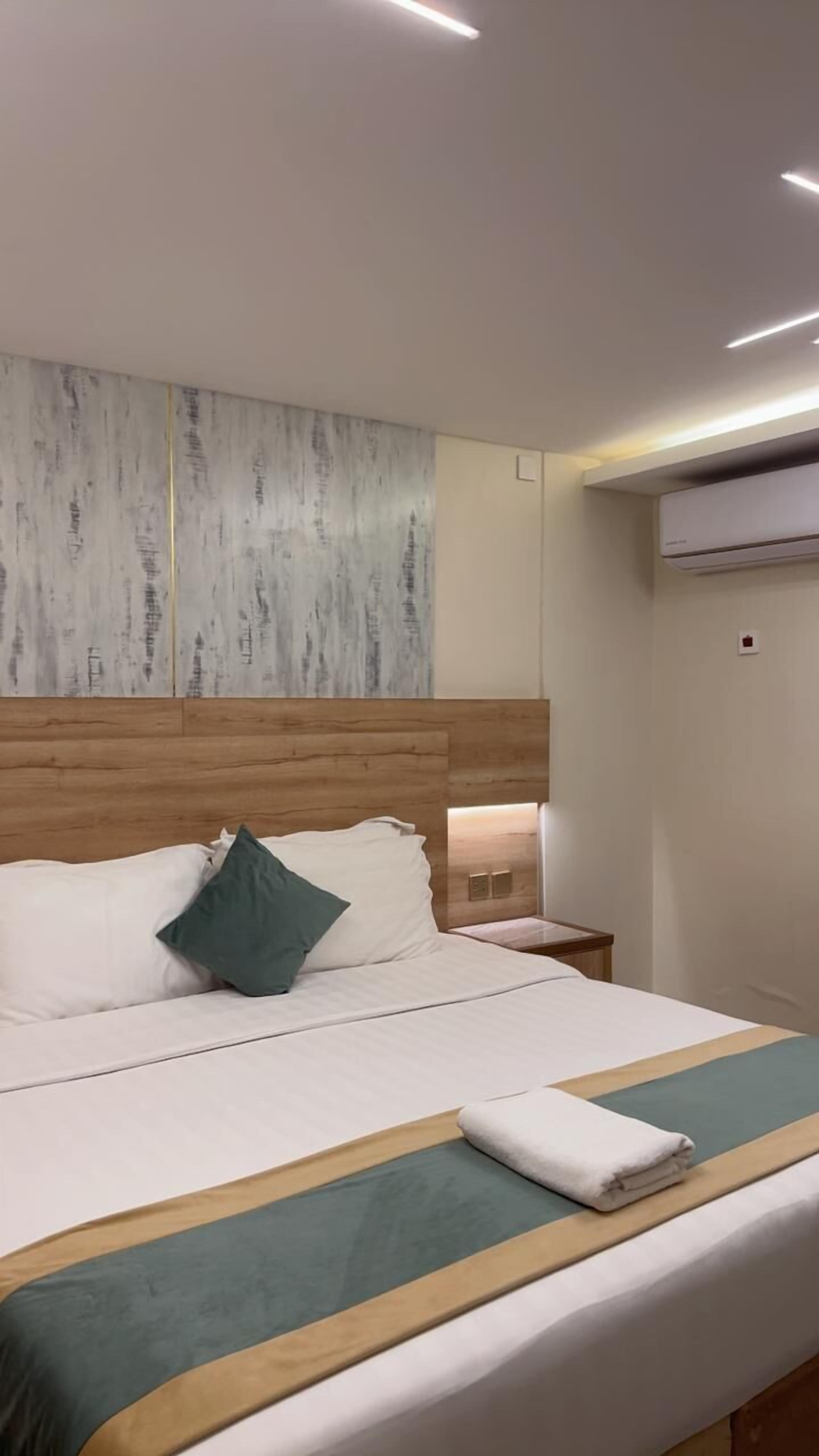 Ein modernes Hotelzimmer mit einem Holzkopfstück, einem großen Bett mit weißer Bettwäsche, einem grünen Kopfkissen und einem Nachttisch mit einer Lampe.
