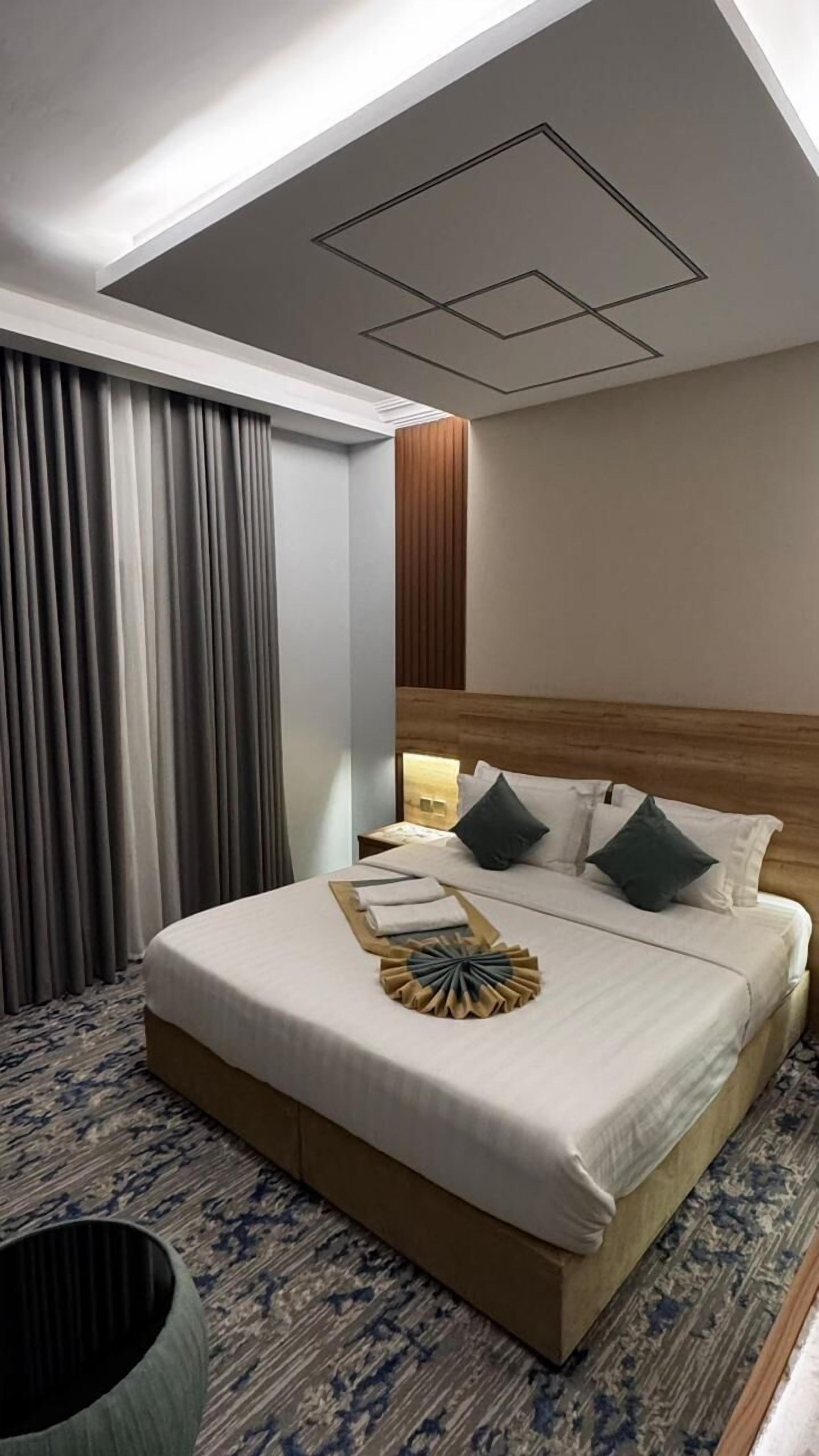 A hotel room with a neatly made bed, a wooden headboard, and a patterned carpet.