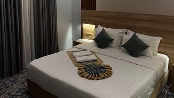 A hotel room with a large bed, a wooden headboard, a nightstand with a lamp, and a ceiling with recessed lighting.