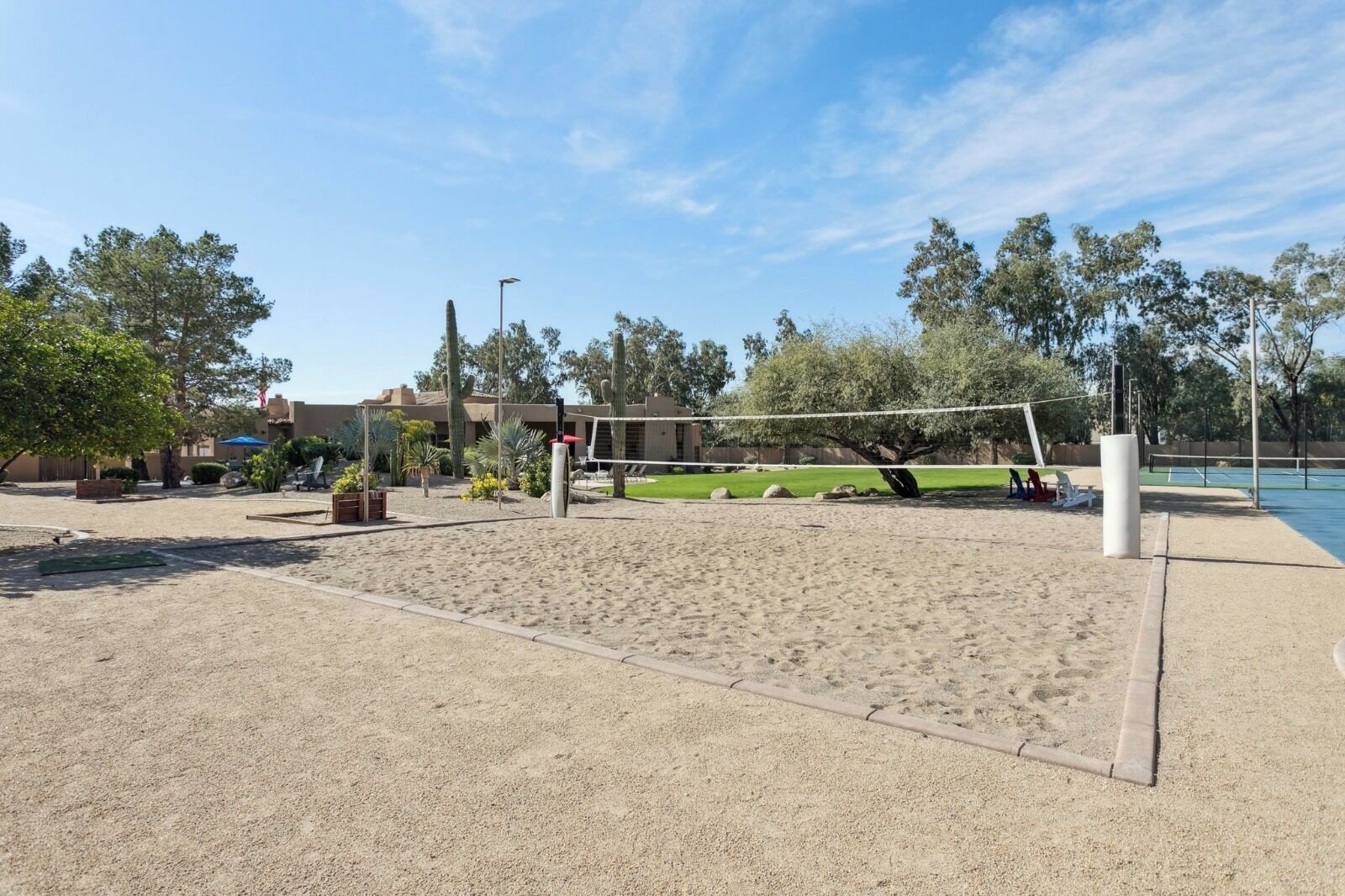 A sandy volleyball court with a net, surrounded by trees and a building in the background.