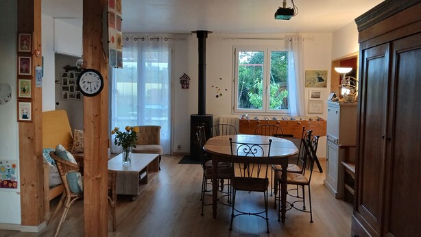 Um quarto aconchegante com piso de madeira, uma mesa redonda com cadeiras, uma lareira e uma janela com cortinas.