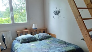 Quarto com cama, escrivaninha, cadeira, radiador, janela e escada de madeira.