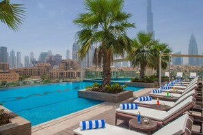 A rooftop pool with lounge chairs and palm trees, overlooking a cityscape with modern buildings. - Maison Privee - Chic Downtown Living w/ Dubai Cityscape Views (Dubai)