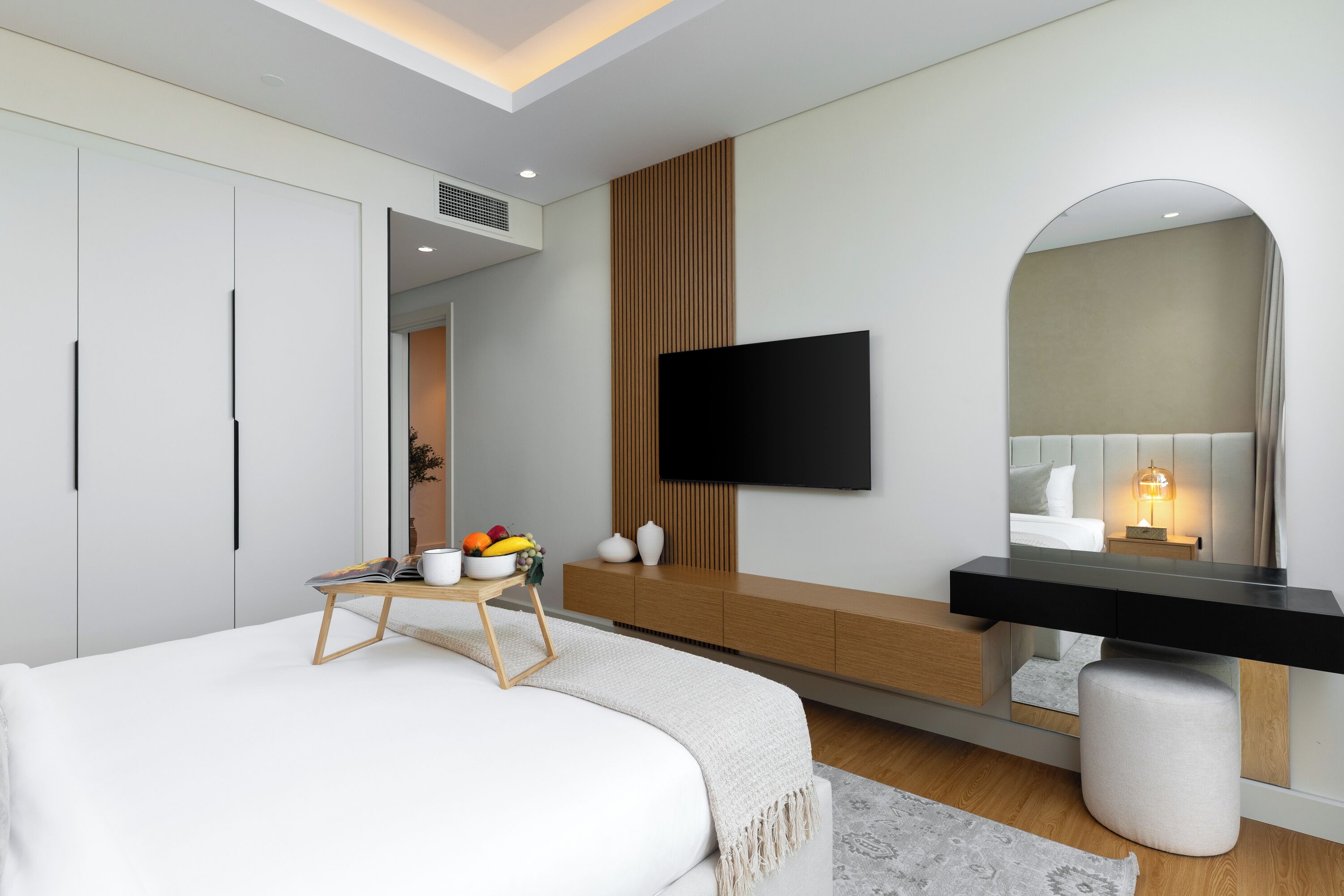 A modern bedroom with a bed, bedside table, fruit bowl, and a TV mounted on the wall.
