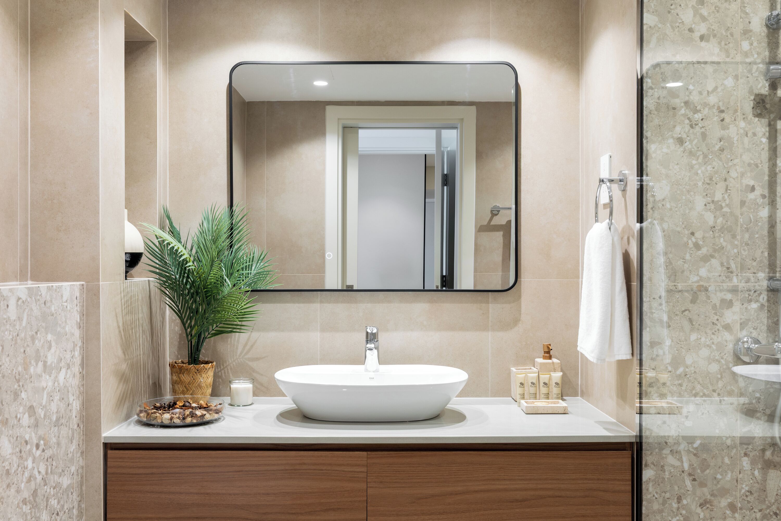 Un baño moderno con un espejo grande, un lavabo redondo, una planta en maceta y una cabina de ducha de vidrio.