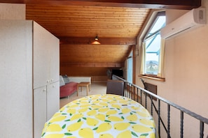 Una habitación con techo de madera, una mesa redonda con estampado de limón, un sofá rojo y una ventana con cortinas.