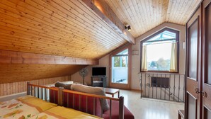 A bedroom with a wooden ceiling, a bed with floral bedding, a red sofa, a TV, and a balcony with a view. - Guest Room Koch with Panoramic View, Private Terrace and Wi-Fi (Bad Säckingen)