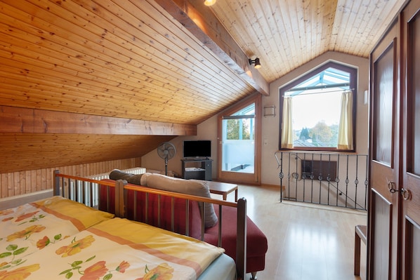 Un dormitorio con techo de madera, una cama con ropa de cama floral, un sofá rojo, un televisor y un balcón con vistas.