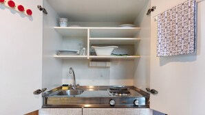 A compact kitchen with a stainless steel sink, a gas stove, and open shelving with dishes and a vase. - Guest Room Koch with Panoramic View, Private Terrace and Wi-Fi (Bad Säckingen)