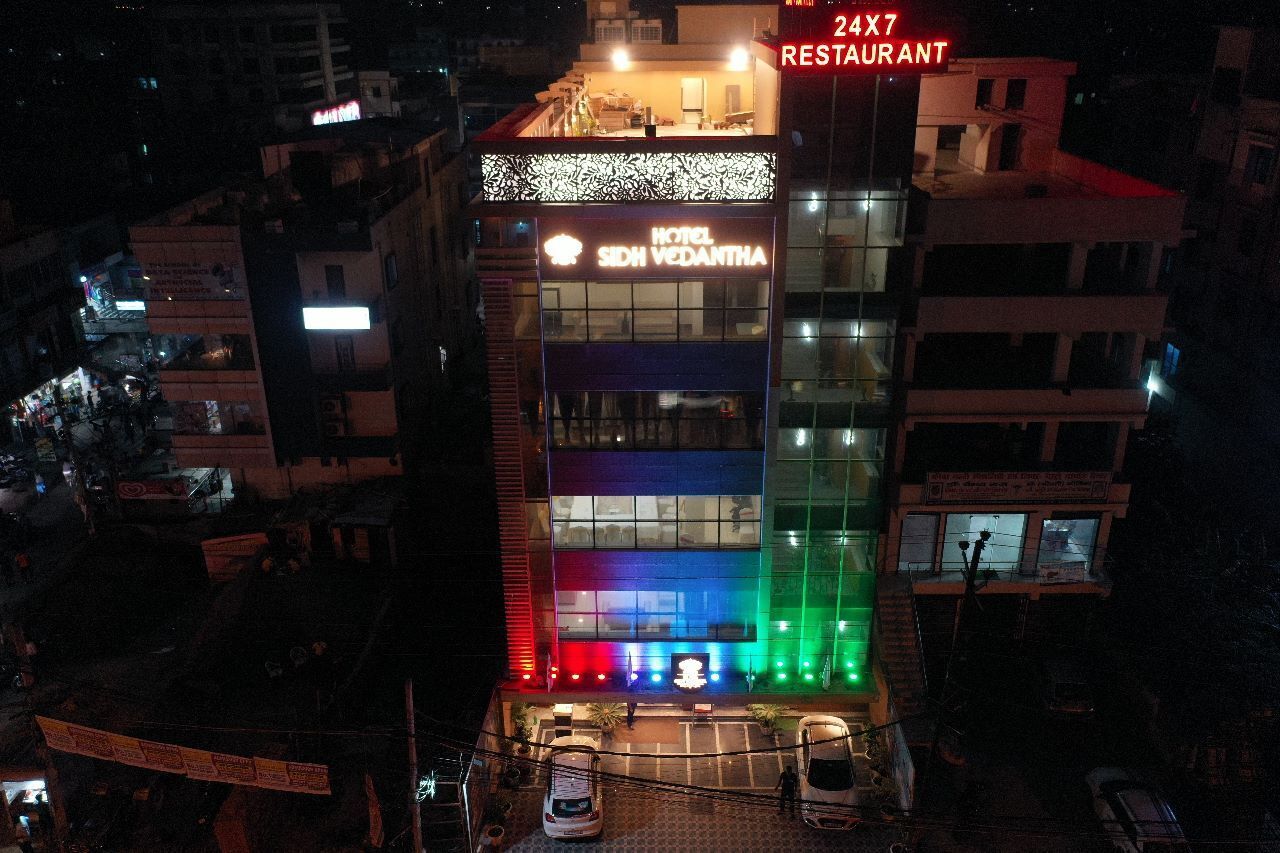 Un hôtel à plusieurs étages, reconnaissable à son enseigne bien visible indiquant « Hôtel Sidh Vedantha » et à son « restaurant ouvert 24 heures sur 24, 7 jours sur 7 » situé au dernier étage.