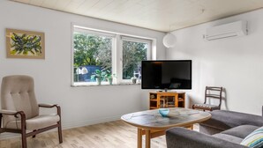Una sala de estar con un sillón color beige, un sofá gris, una mesa de centro de madera y un televisor de pantalla plana sobre un mueble.