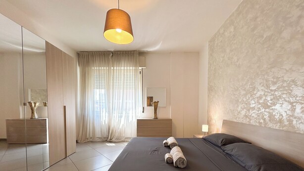 Une chambre à coucher moderne avec un grand lit, une table de chevet, un miroir et un luminaire suspendu.
