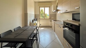 Une cuisine moderne avec un coin repas, dotée d’une grande fenêtre, d’appareils électroménagers intégrés et d’un luminaire suspendu.