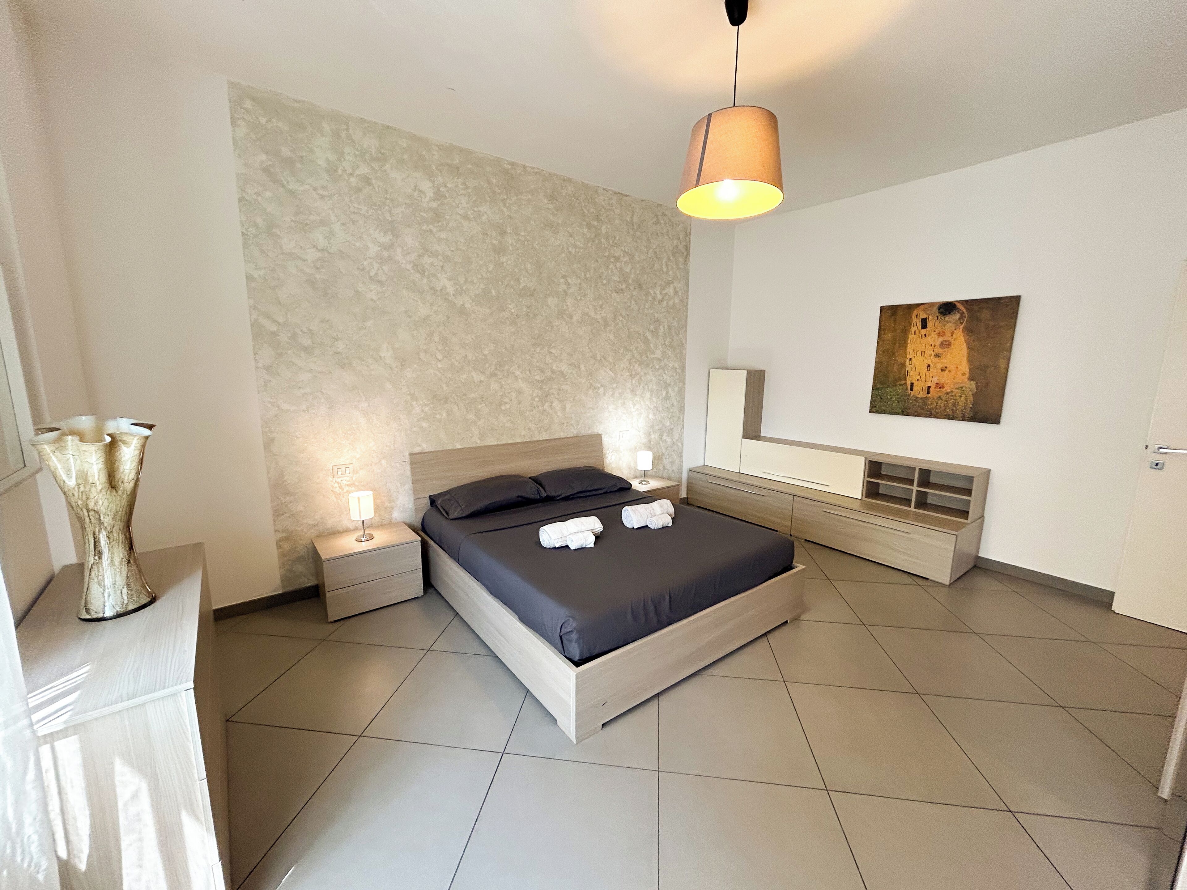 Une chambre à coucher moderne avec un lit, des tables de chevet, une lampe, un tableau et un vase.