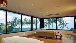 A bedroom with a large bed, a sofa, and a view of palm trees and the ocean. - Saba Estate Luxury Villa Bali (Bali)