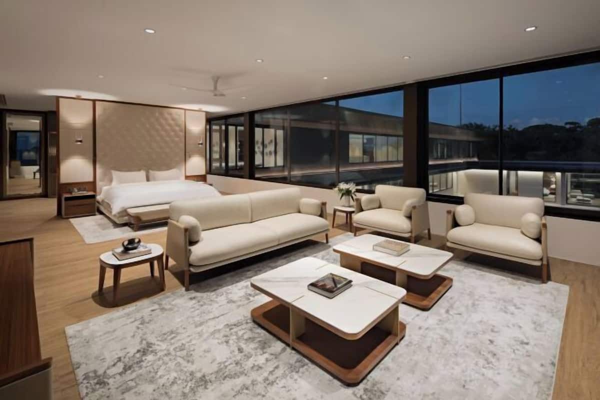 A modern hotel room with a large bed, two sofas, two coffee tables, and a large window with a city view.