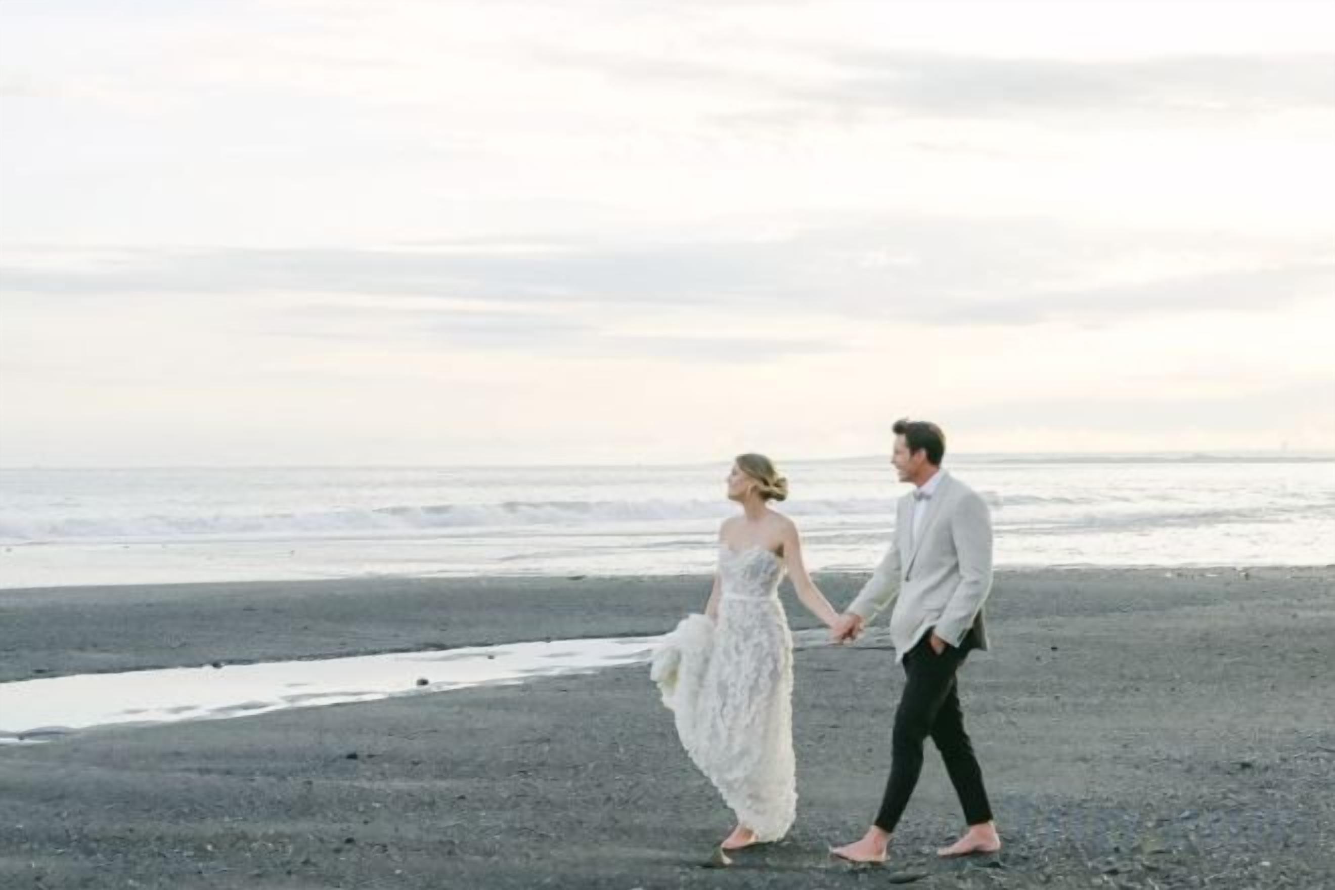 A couple walking on a beach with the ocean in the background.