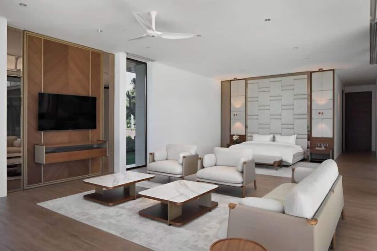 A modern hotel room with a large bed, a TV, a seating area with sofas and a coffee table, and a large mirror.