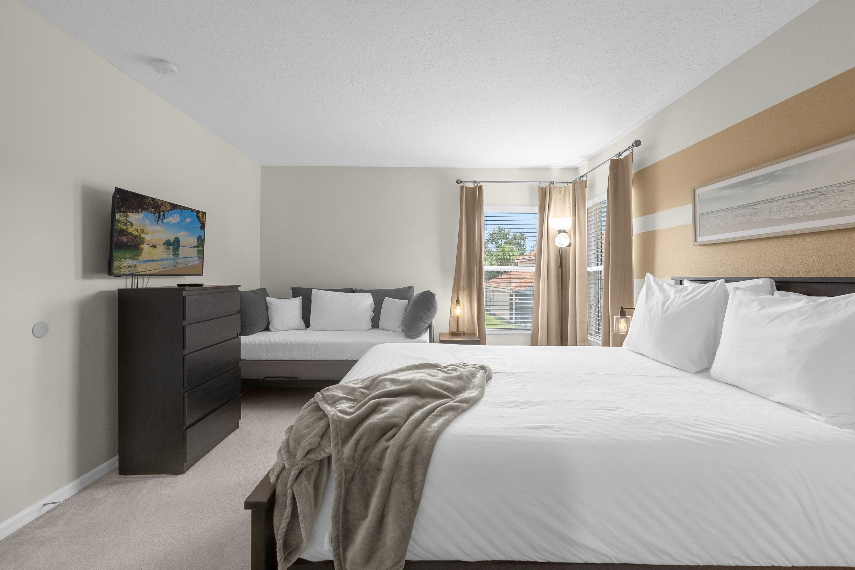 A bedroom with a large bed, a smaller bed, a dresser, and a painting on the wall.