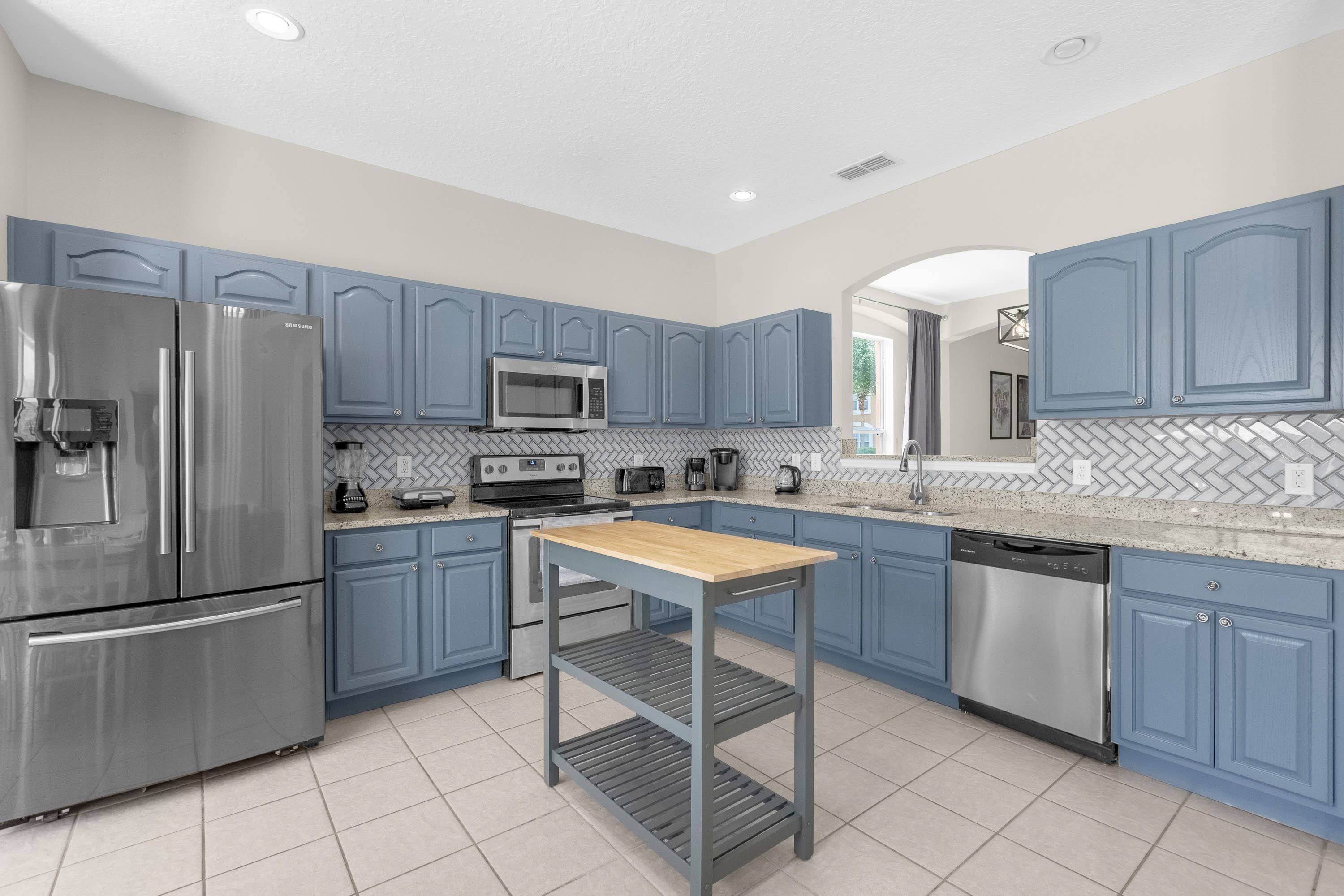 A modern kitchen with blue cabinets, stainless steel appliances, and a wooden table.